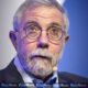 "Imagem de Paul Krugman em evento público, economista olha para a câmera com expressão crítica."